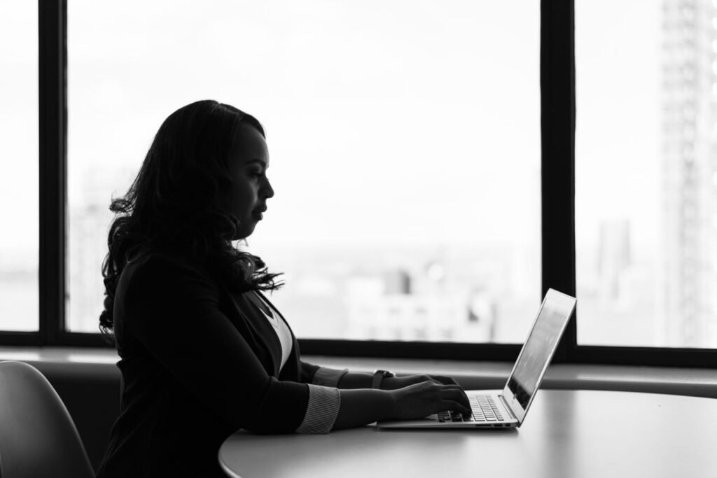 Black and white image of a woman working on her laptop in a modern office setting.