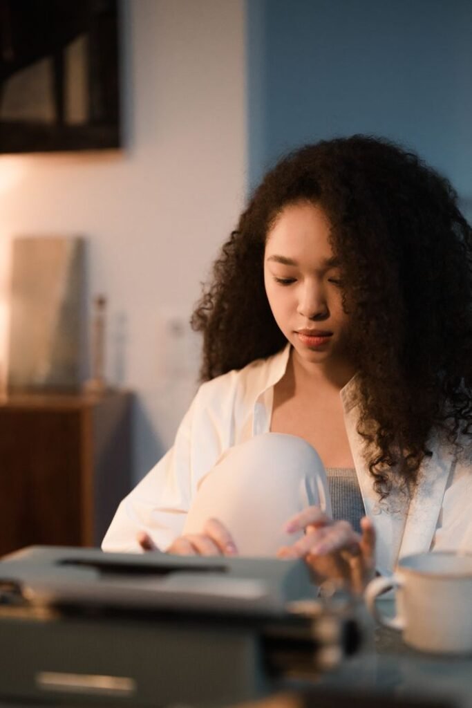 A focused woman with curly hair types on a typewriter in a warmly lit indoor setting, creating content.
